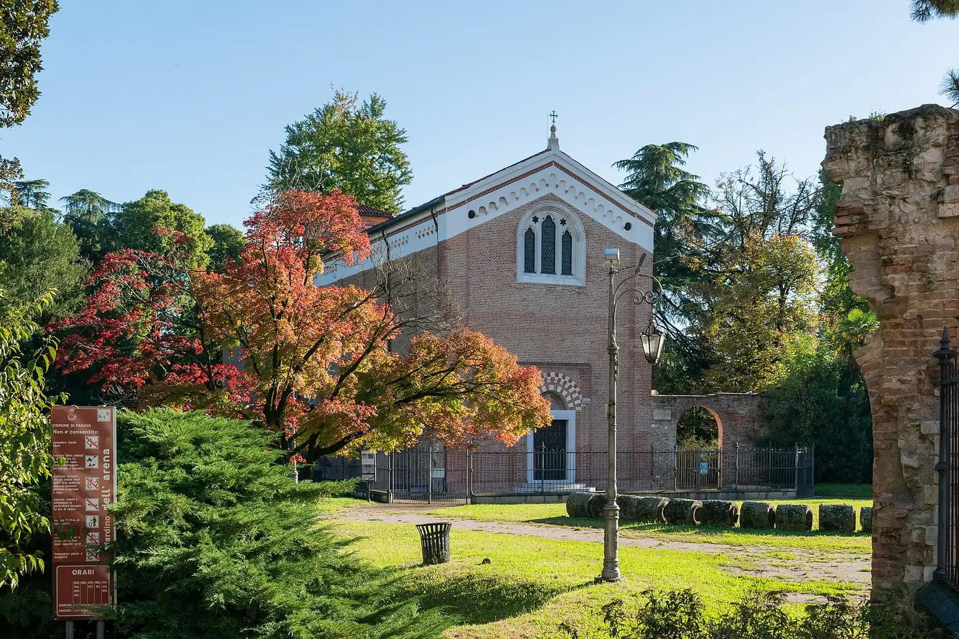 Die schlichte Ziegelfassade der Scrovegni-Kapelle zwischen Bäumen in den Gärten der Arena von Padua